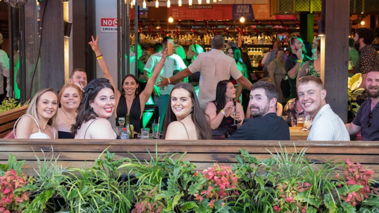 People socialising in the vibrant outdoor seating area of The General Assembly, adorned with plants and atmospheric lighting, perfect for private hires and casual gatherings.