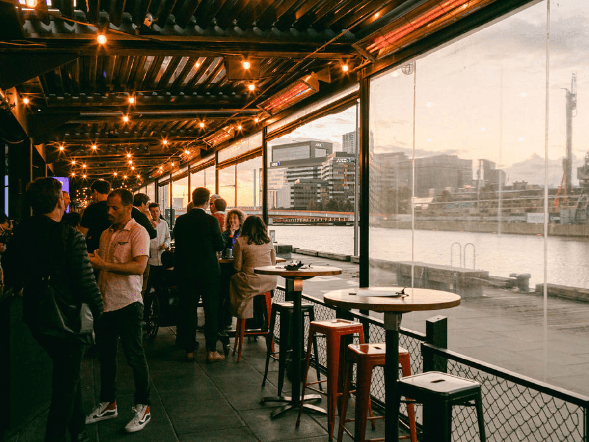 a group of people sitting at tables and chairs in a room with a river and city view